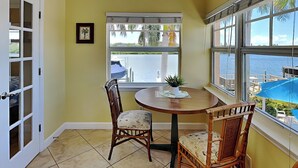 A room with a round table, two wicker chairs, a window with a view of the sea, and a door with frosted glass panels. - Water View Condo Across from Beach + Access to Amenities (Indian Shores)