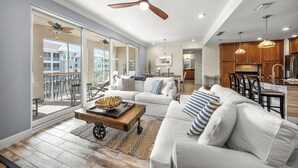 A spacious living area with a large sliding glass door leading to a balcony, a ceiling fan, and a kitchen area with wooden cabinets and pendant lighting. - Waterfront Condo with Lanai and Pool, Near AMI Beaches and Marina (Bradenton)