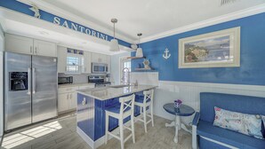 A kitchen with a central island, white cabinets, stainless steel appliances, and a blue accent wall. - Greek-Inspired Cottage: Deck Views, Walk to Beach and Shops (Bradenton Beach)