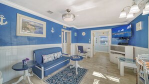 A room with a blue and white color scheme, featuring a sofa, a small table, a chair, a television, and a ceiling fan. - Greek-Inspired Cottage: Deck Views, Walk to Beach and Shops (Bradenton Beach)