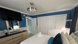 A bedroom with a bed, a dresser, a mirror, a ceiling fan, and a TV. - Greek-Inspired Cottage: Deck Views, Walk to Beach and Shops (Bradenton Beach)