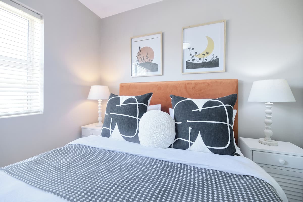Un dormitorio ordenado con una cama, dos mesitas de noche y decoración en la pared.