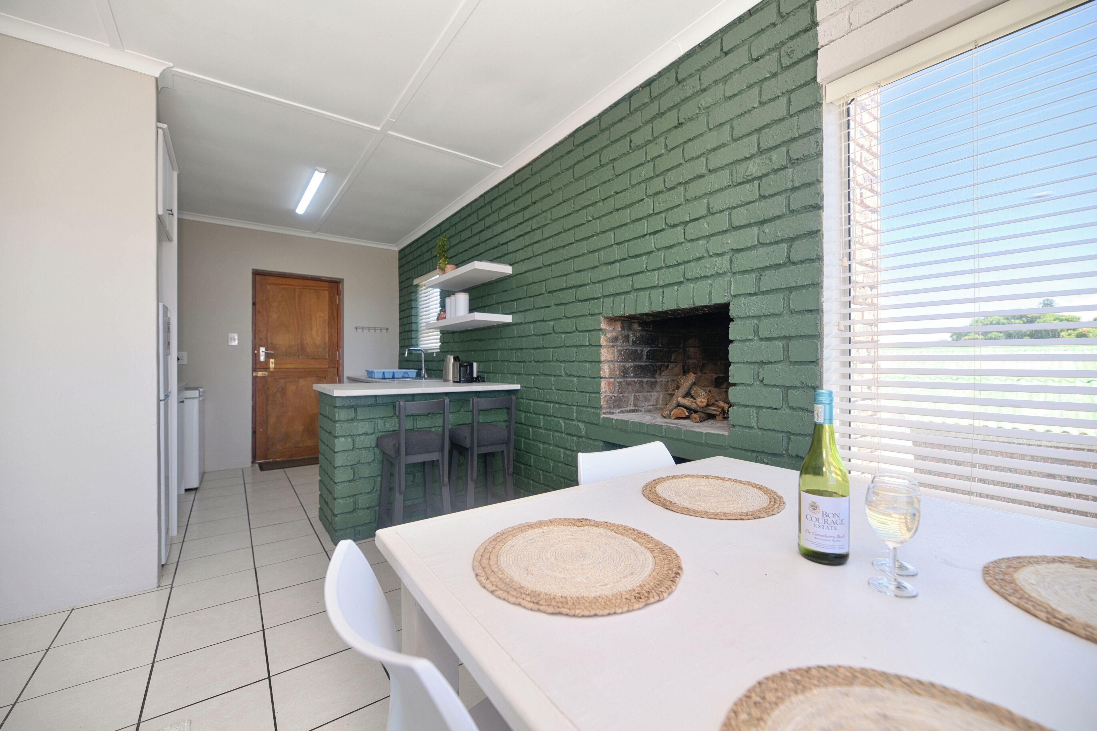 A dining area with a brick wall, a fireplace, and a table set with placemats and a bottle of wine.