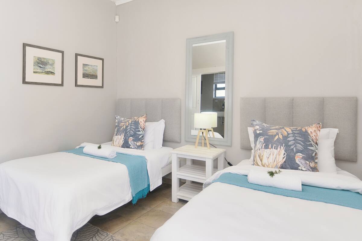 Habitación de hotel con dos camas, una mesita de noche con lámpara y cuadros en la pared.