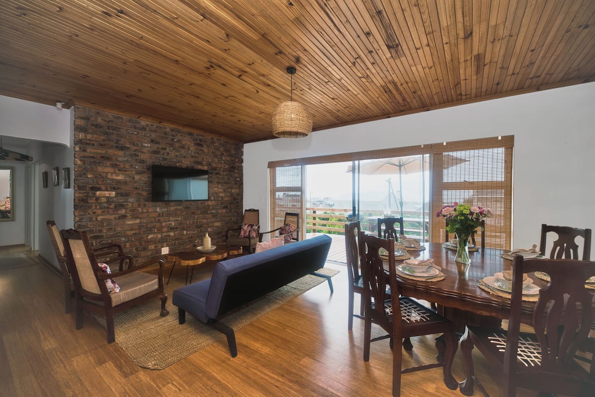 Una sala de estar moderna con pared de ladrillo, techo de madera y un ventanal grande.