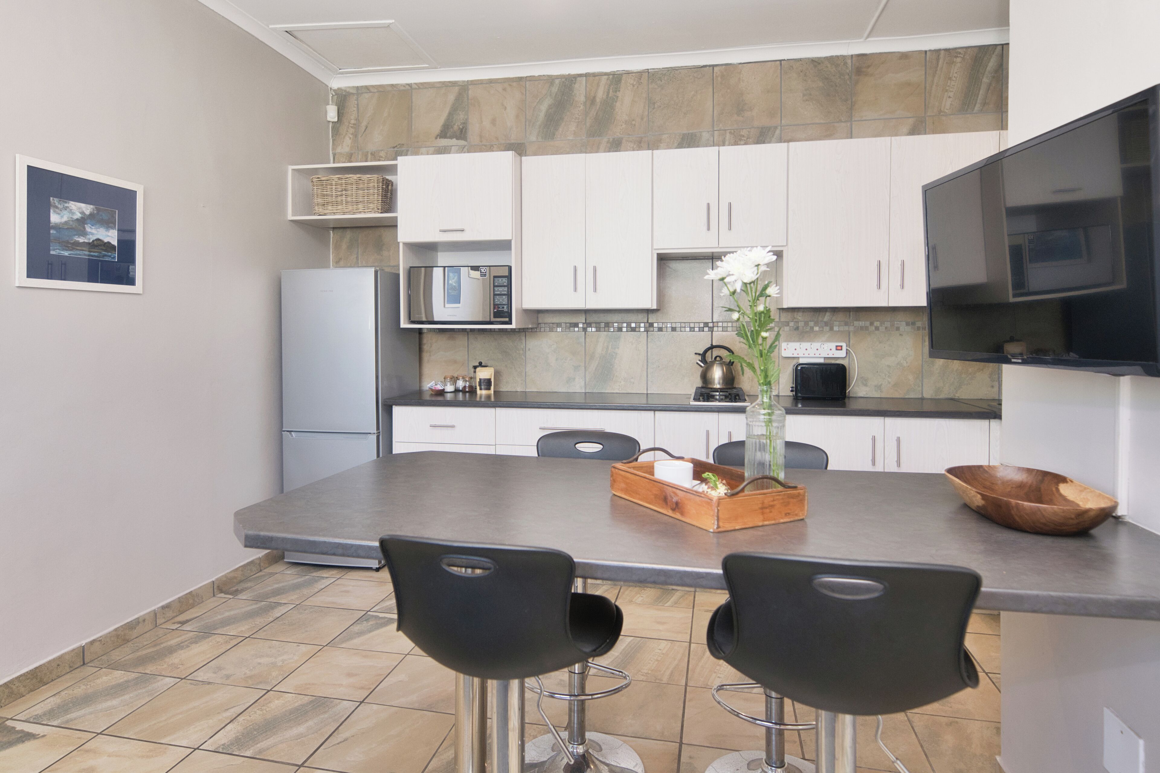 Una cocina moderna con armarios blancos, una isla grande con taburetes, un refrigerador, microondas y un televisor.