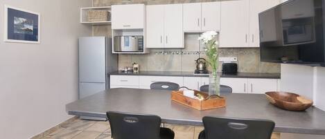 Una cocina moderna con armarios blancos, una isla grande con taburetes, un refrigerador, microondas y un televisor.