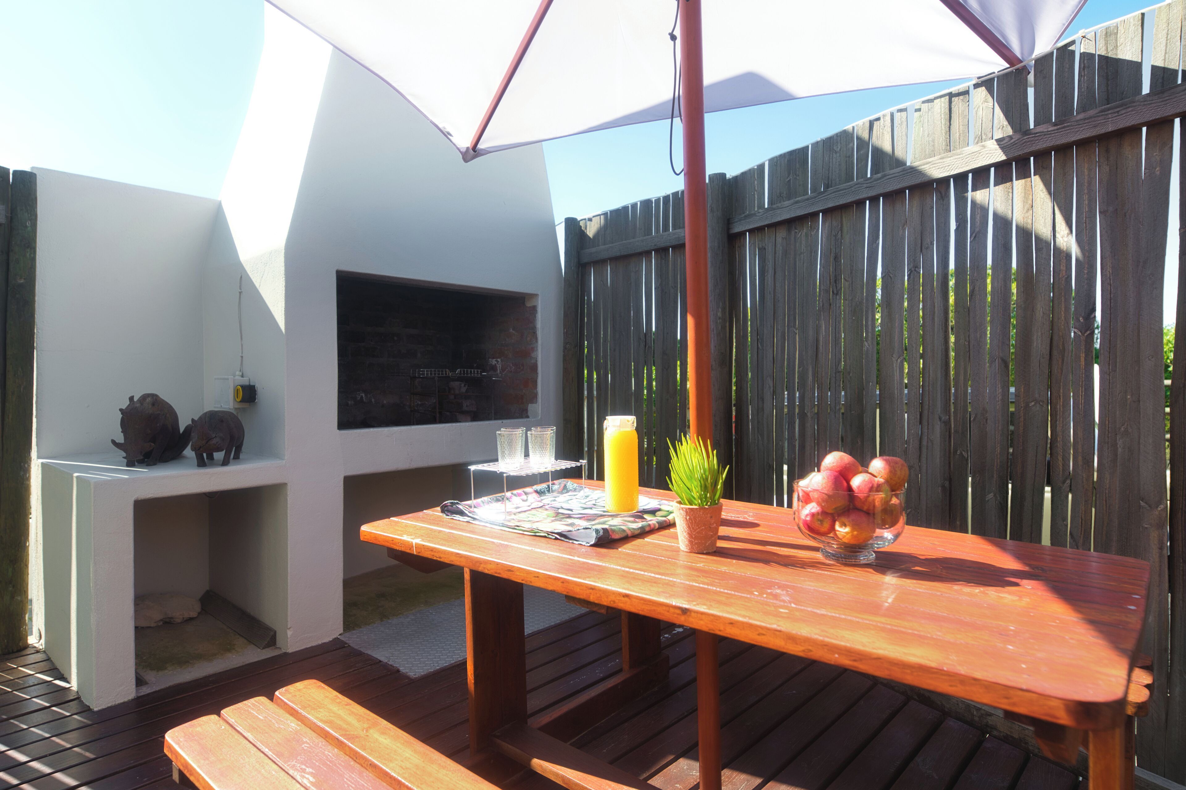A wooden deck with a table, a bench, a potted plant, a fruit bowl, and a beverage.