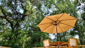 Una terrazza esterna con tavolo e sedie di legno, un ombrellone grande e un recinto in legno.