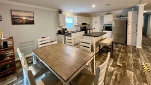 Una cucina moderna con mobili bianchi, un'isola centrale e una zona pranzo con tavolo in legno e sedie bianche.