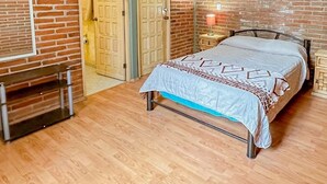 A bedroom with a wooden floor, a bed with a patterned bedspread, two doors, a bench, and a wall clock. - New Family House. Pool & BBQ Area (Yautepec)