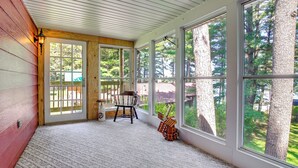 A covered porch with large windows, a wooden bench, and a small table. - Waterfront Berry Lake Getaway w/ Sunroom! (Gillett)