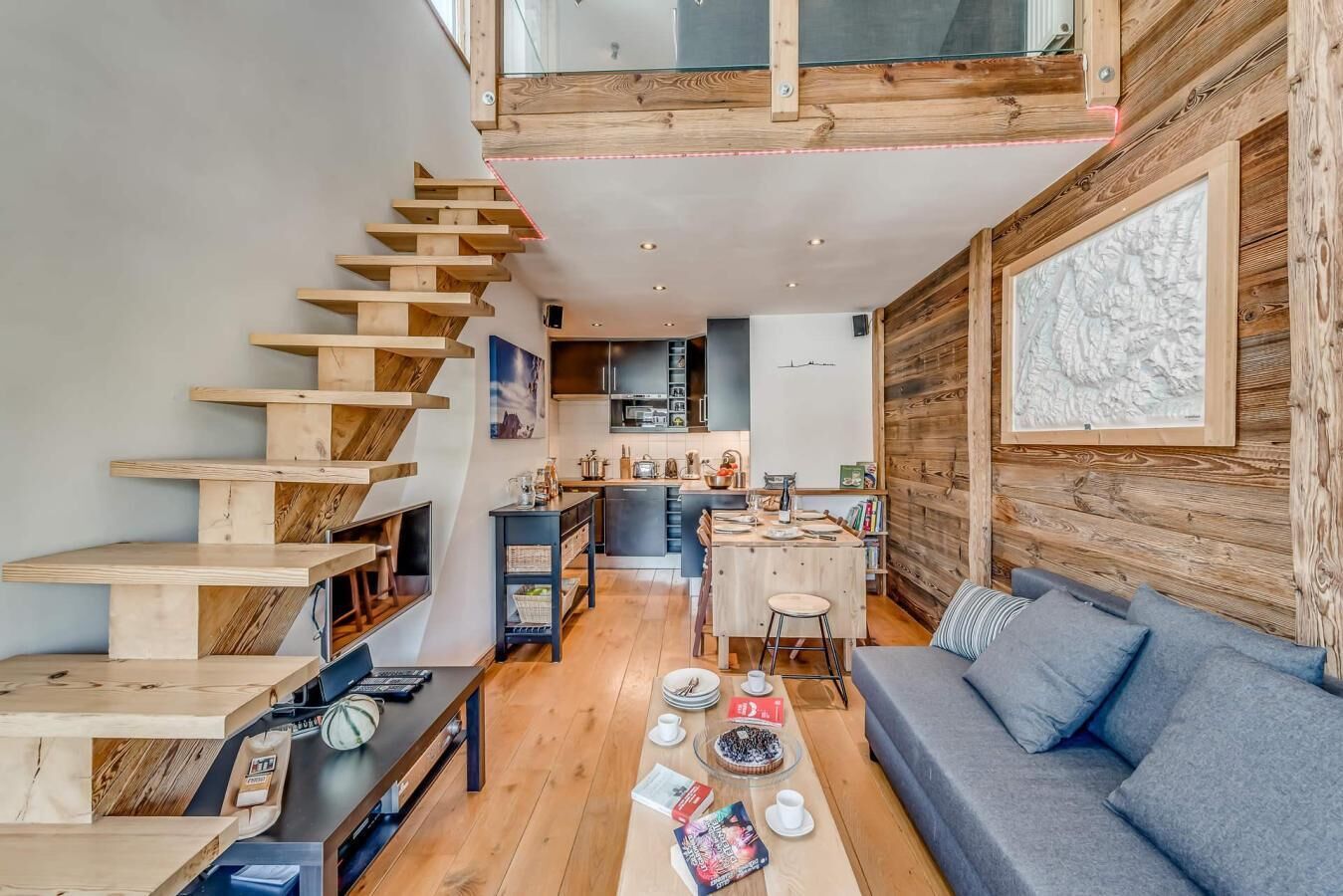 A modern interior with a wooden staircase, a kitchen, and a living area with a sofa and coffee table.