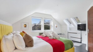 A bedroom with a sloped ceiling, a bed with white bedding, a red and green throw, and a television on a stand.