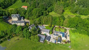 An aerial view of a residential area with multiple houses, a large open field, and a dense forest in the background.