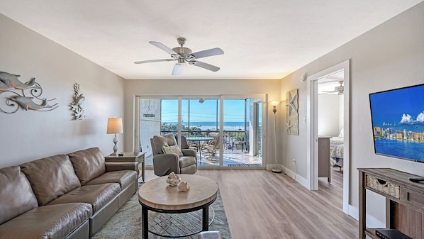 A spacious living room with a leather sofa, a round coffee table, and a ceiling fan. - Amazing Gulf Views 2 Bed 2 Bath at Siesta Key Beach Steps to Beach (Siesta Key)