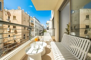 A balcony with white furniture, including a sofa and two round tables, under a large window. - MAMAD - Shenkin Eclectic Blue Apt by Sea N' Rent (Tel Aviv)