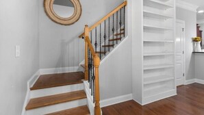 Una escalera de madera con escalones y barandilla, que conduce a un espacio interior blanco con un espejo circular en la pared.
