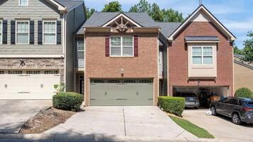 A two-story residential building with a brick facade, a central garage door, and a driveway leading to a parked SUV.