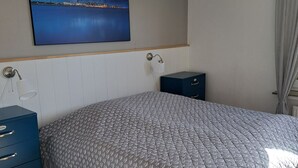 Et soveværelse med seng, kommode, natbord, væglampe og et maleri af et kystlandskab.