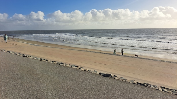 En strand med en anlagt sti, gelænder og havet.