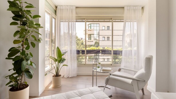 A modern room with a large window, a potted plant, a white sofa, and a small table. - Heart of TLV Elegant Home by Sea N' Rent (Tel Aviv)