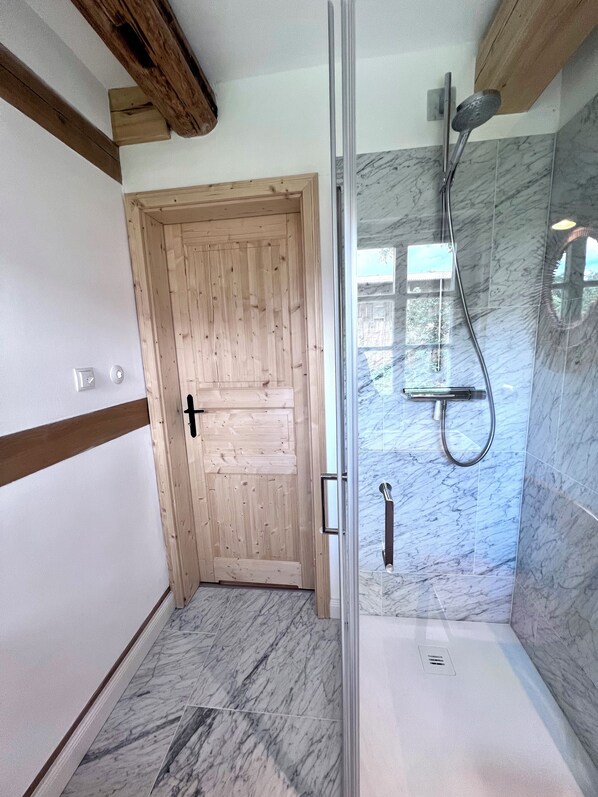 Un baño con puerta de madera, ducha con cabezal de mano y suelo de mármol.