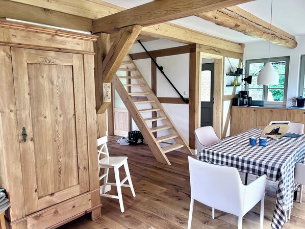 A rustic interior with a wooden staircase, a dining area with a checkered tablecloth, and a large wooden cabinet.