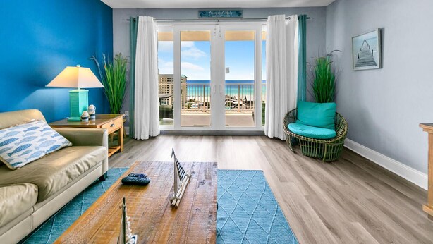 Een woonkamer met uitzicht op het strand, een bank, een tafel met een lamp en een rieten stoel.