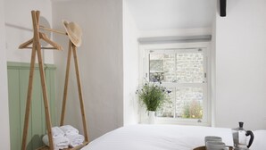 A bedroom with a bed, a wooden drying rack, a window with a view of a stone building, and a tray with a coffee maker. - Bridge House -  a house that sleeps 6 guests  in 3 bedrooms (Newlyn)