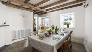 A dining area with a table set for four, wooden beams on the ceiling, a white radiator, and a window with a view of the street. - Bridge House -  a house that sleeps 6 guests  in 3 bedrooms (Newlyn)