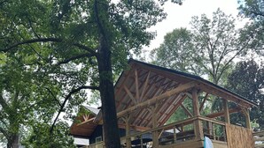 Een houten constructie met een overdekt terras, omgeven door bomen en een grindpad.