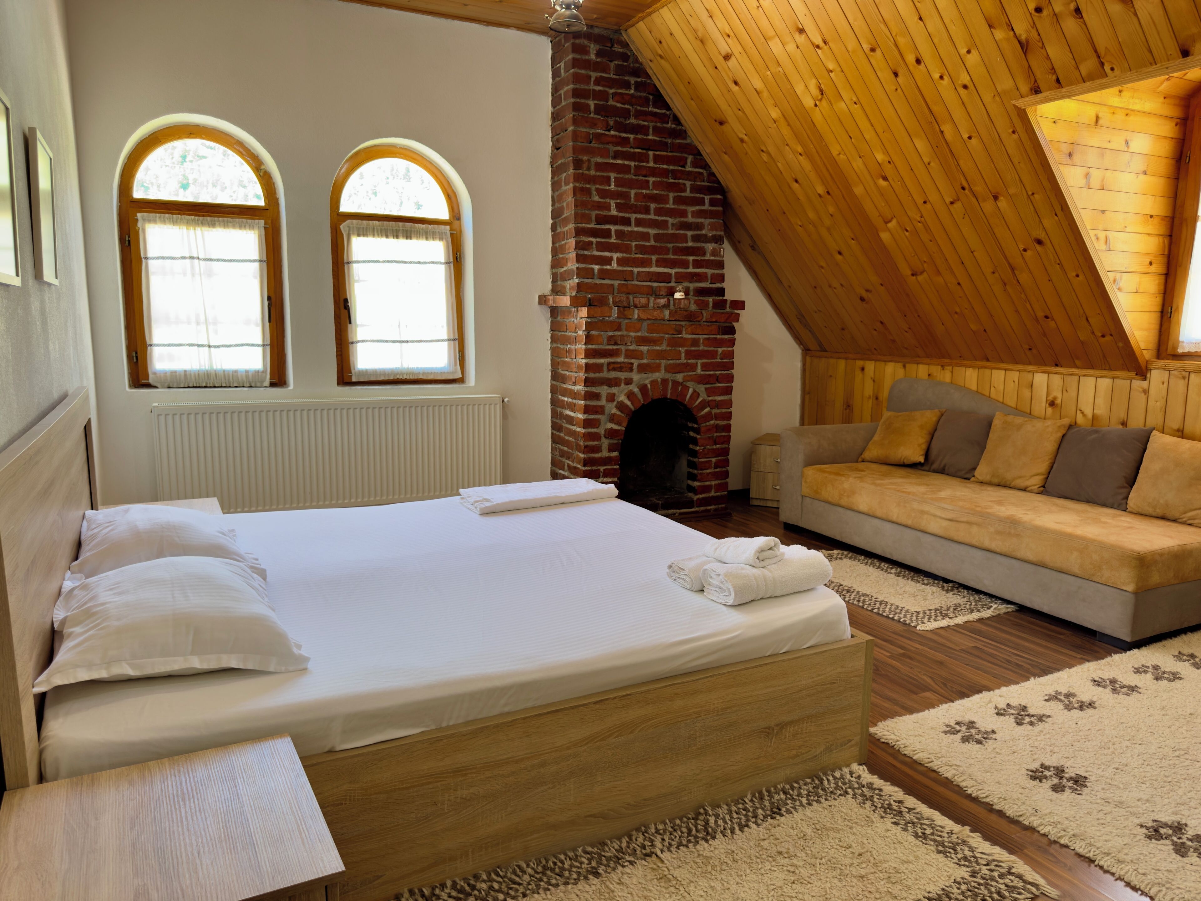 A bedroom with a wooden bed, a sofa, a fireplace, and two arched windows.