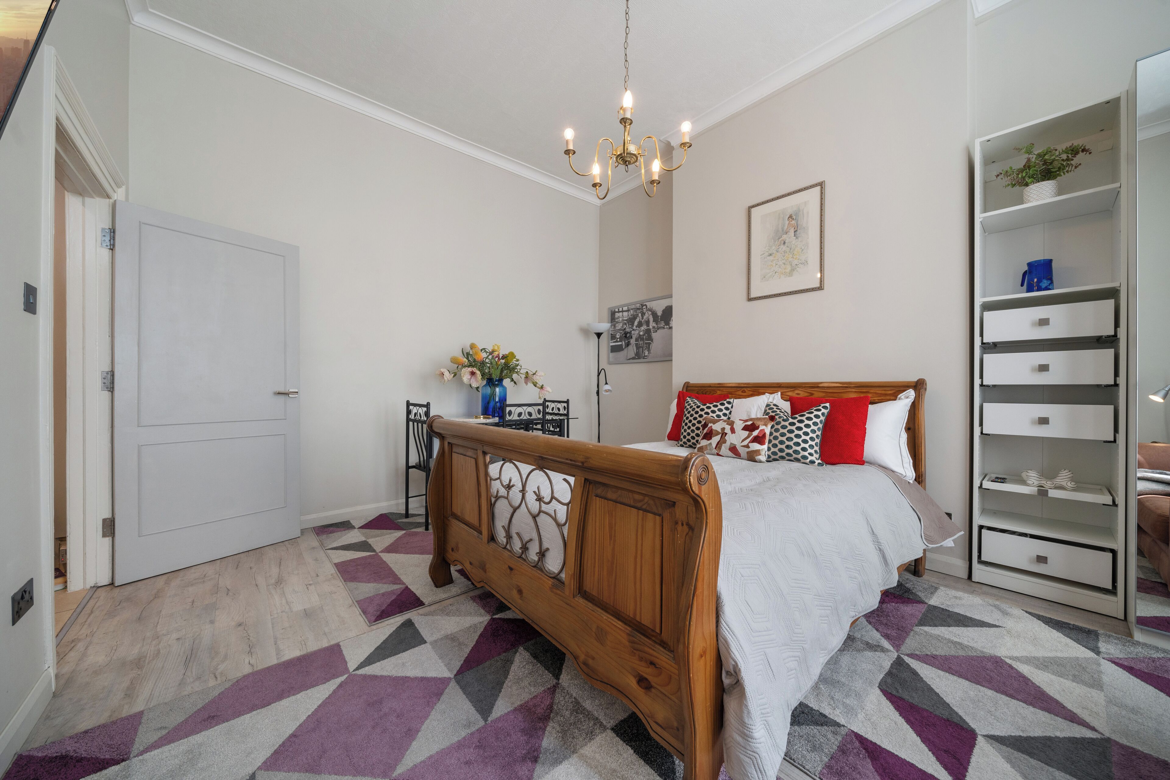 A bedroom with a wooden bed, a white wardrobe, and a patterned rug.