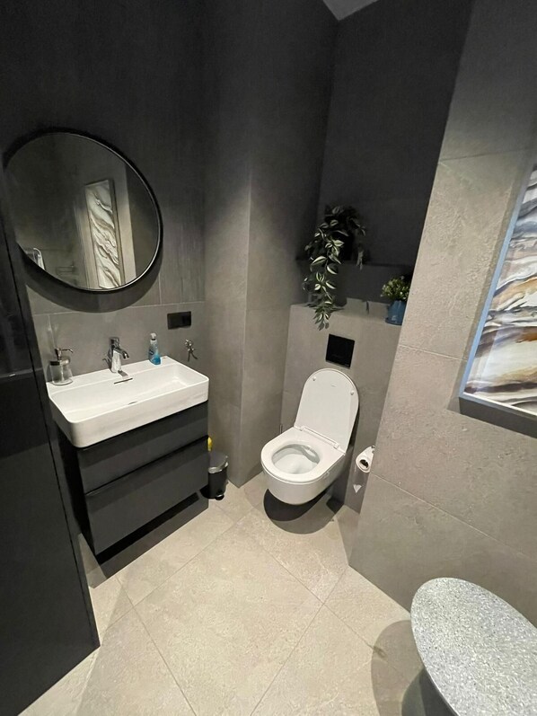 A modern bathroom with a round mirror, white sink, and toilet.