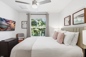 Quarto de hotel com cama, escrivaninha, cadeira, ventilador de teto e janela com persianas.