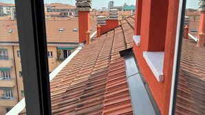 Une vue depuis une fenêtre donnant sur un paysage urbain, avec des toits recouverts de tuiles en terre cuite et des bâtiments rouges.
