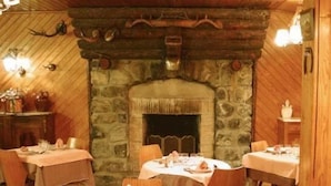 A rustic dining area with stone walls, wooden beams, and a fireplace. Tables are set for dining. - Hotel Las Donnas (Saint-Etienne-de-Tinee)