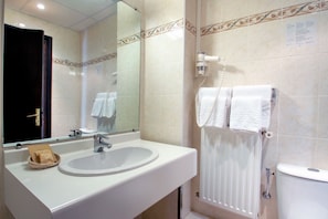 Un baño con lavamanos, espejo, toallero y retrete.