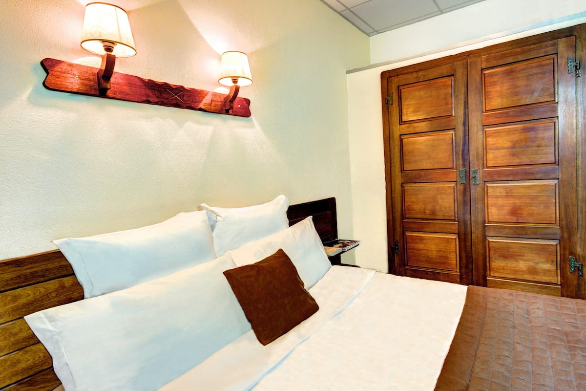 A hotel room with a bed, two bedside lamps, a wooden headboard, and a wooden wardrobe.
