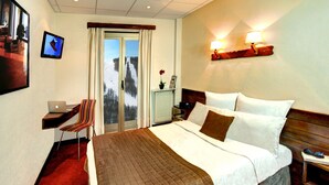 A hotel room with a bed, a desk with a laptop, a chair, a window with a view of a snowy landscape, and a wall-mounted lamp. - Hotel Las Donnas (Saint-Etienne-de-Tinee)