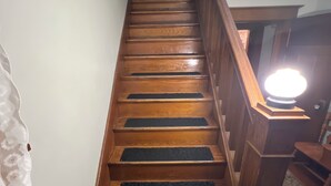 Una escalera de madera con barandilla, escalones alfombrados y un accesorio de iluminación en la parte superior.