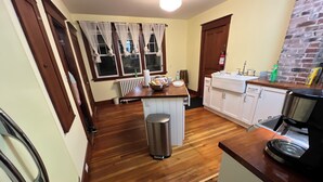 Cocina con suelo de madera, cafetera, pileta y ventana con cortinas.