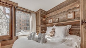 A bedroom with a large bed, wooden walls, a window with curtains, and a teddy bear on the bed. - 100m from ski slopes, balcony, tv, ski locker, 56m², Tignes (Tignes)