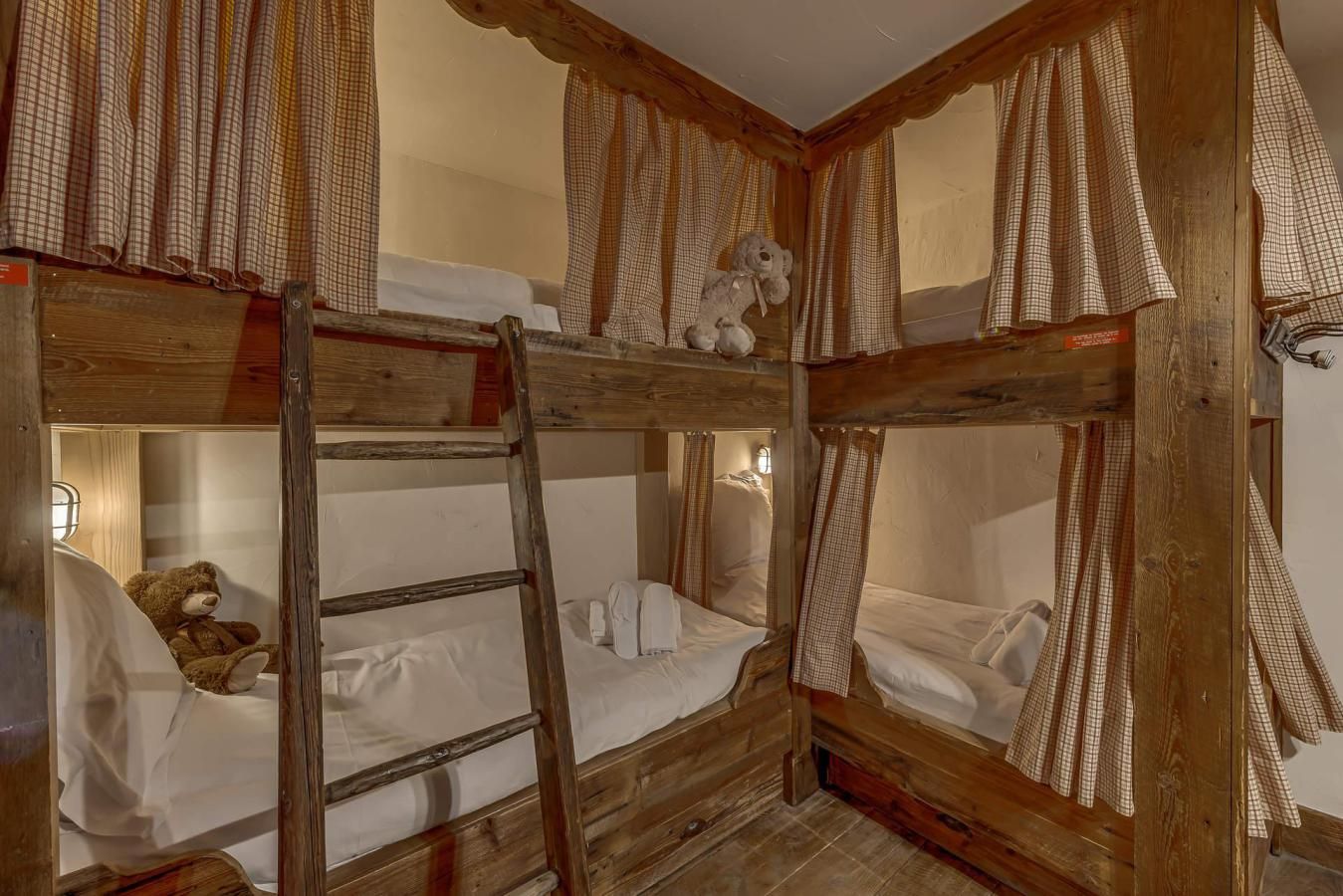 A rustic wooden bunk bed room with a ladder, a teddy bear, and a checkered curtain.