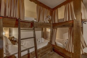 Ein rustikales Schlafzimmer mit Etagenbetten aus Holz, einer Leiter, einem Teddybären und einem karierten Vorhang.