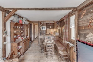 A rustic kitchen with wooden beams, a dining area with a bench, and a TV mounted on the wall.