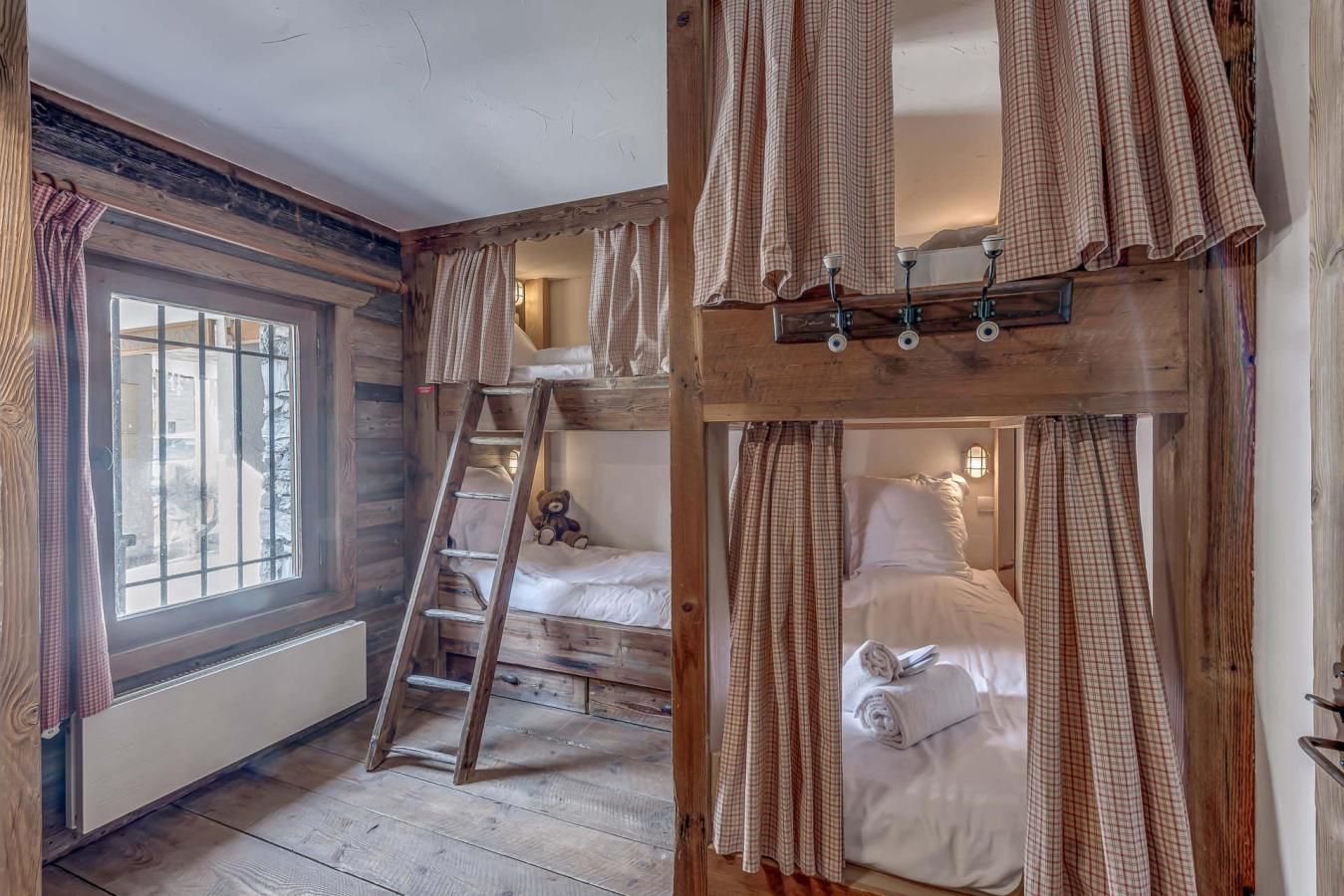 Una habitación rústica con literas, una escalera, una ventana con cortinas y techo de madera.