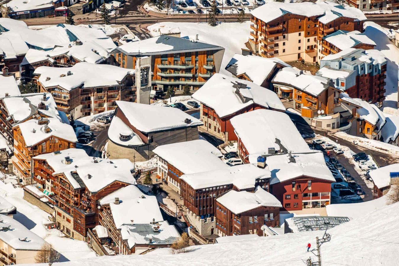 A snow-covered town with multiple buildings, including a prominent hotel with balconies and a ski lift in the background.