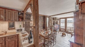 A rustic kitchen with wooden cabinets, a dining table, and chairs. There is a wooden ceiling and a view of the outside through large windows. - 100m from ski slopes, balcony, tv, ski locker, 56m², Tignes (Tignes)